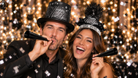 Couple celebrating New Year's Eve in a black Happy New Year top hat and black feather tiara with black foil horns from the Blackout New Year Party Kit