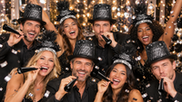 Friends celebrating New Year's Eve in black Happy New Year top hats and feather tiaras from the Blackout New Year Party Kit, blowing black foil horns